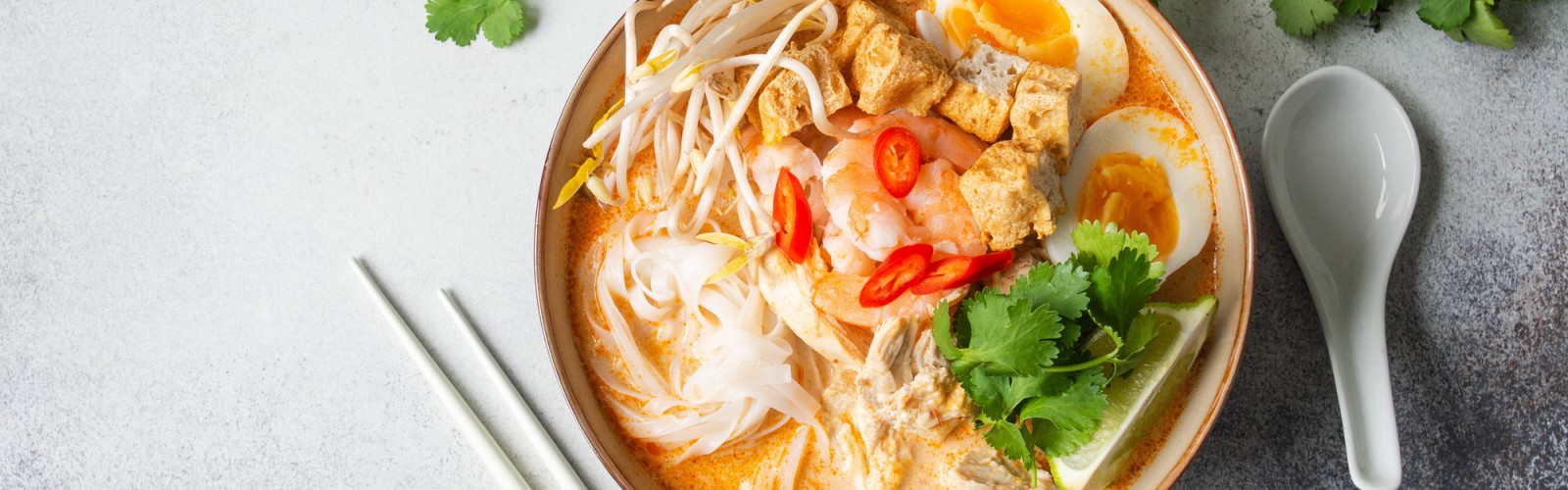 Malaysian noodles laksa soup with chicken, prawn and tofu in a bowl on grey background. Top view. Copy space
